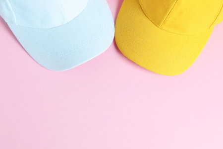 White and yellow baseball hats on pink background, top view. Space for text