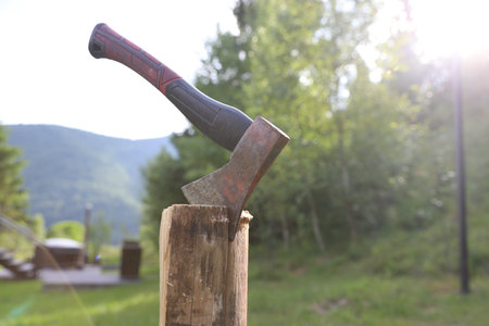 Metal ax on wooden log outdoors, closeup. Space for text
