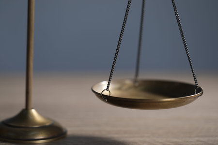 Scales of justice on wooden table against grey background, closeup