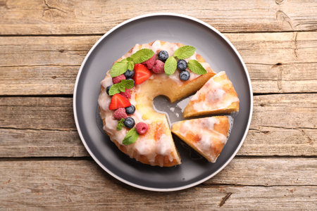 Pieces of bundt cake with berries, glaze and mint on wooden table, top view