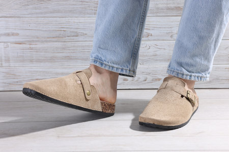 Woman in stylish beige slippers on light wooden floor, closeup