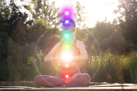 Woman meditating in Lotus pose in nature. Seven chakras glowingの写真素材