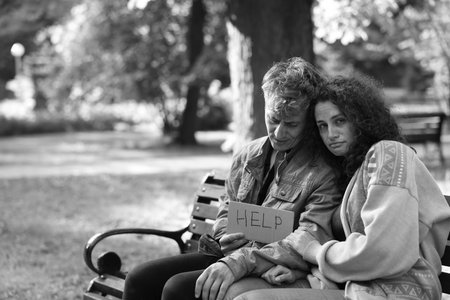 Homeless people with sign Help on bench in park, space for text. Black and white effectの写真素材