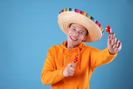 Happy man in sombrero hat playing maracas on light blue background