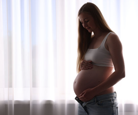 Beautiful pregnant woman near window at home. Space for text