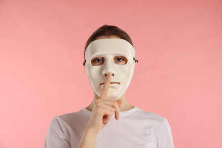 Anonymity. Woman wearing mask and showing hush gesture on pink backgroundの写真素材