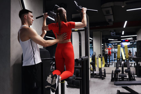 Young woman exercising with professional personal trainer in gym, back view. Space for text