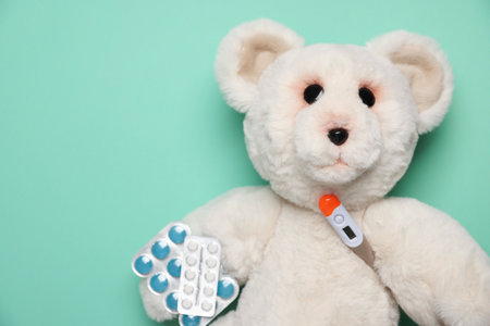 Pediatrics concept. Toy bear with thermometer and pills on turquoise background, top view. Space for textの写真素材