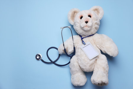 Pediatrics concept. Toy bear with stethoscope on light blue background, top view. Space for textの写真素材