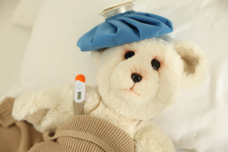 Pediatrics concept. Toy bear with ice bag and thermometer in bedの写真素材