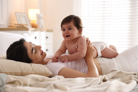 Mother with her cute little baby on bed indoors