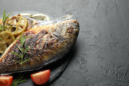Homemade seafood dish. Tasty roasted dorado fish with spices and tomato on black table, closeup....