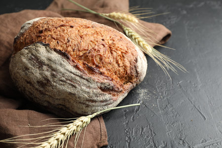 Loaf of fresh bread and spikes on black table, closeup. Space for text