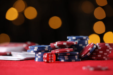 Casino chips, playing cards and die on red table against blurred lights, closeup