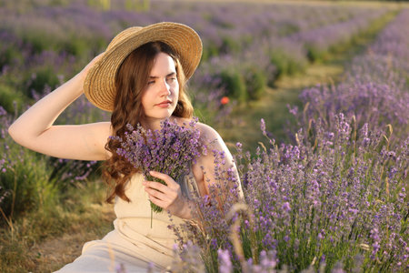 Beautiful young woman with lavender flowers in fieldの写真素材