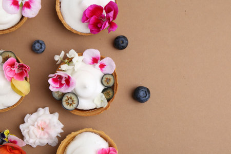 Delicious dessert. Tartlets with cream, berries and flowers on light brown background, flat lay....