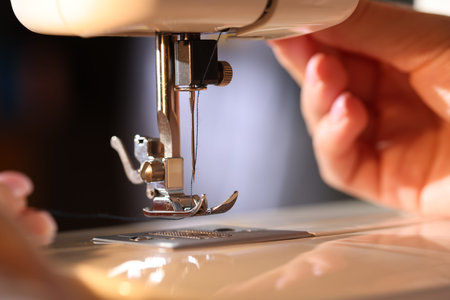 Woman threading sewing machine needle on blurred gray background, macro view