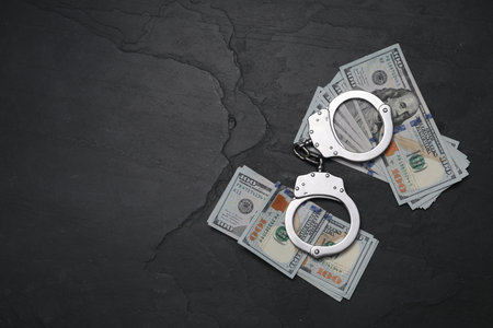 Corruption. Handcuffs and dollar bills on black table, flat lay. Space for textの写真素材