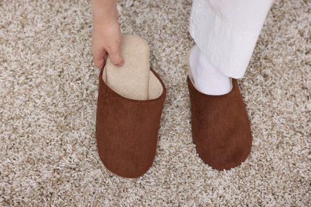 Woman wearing brown slippers on soft beige carpet, above view