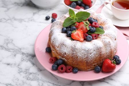 Tasty Bundt cake with powdered sugar and berries on white marble table, closeup. Space for textの写真素材