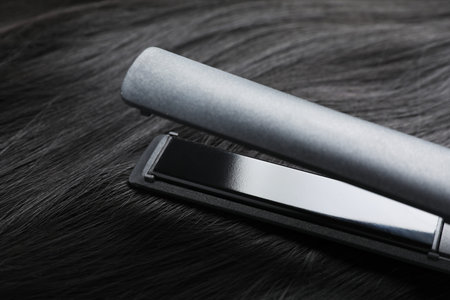 Modern flat iron on shiny black hair, closeup