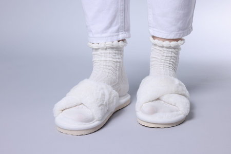 Woman in fluffy white slippers on grey background, closeup