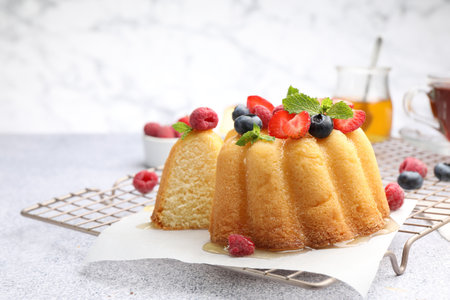 Tasty Bundt cake with berries and mint on light grey table, closeup