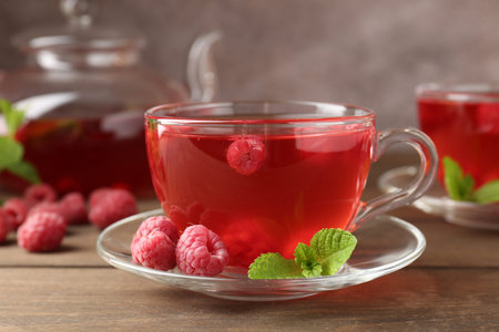 Tasty raspberry tea in glass cups, teapot, berries and mint on wooden table, closeupの写真素材