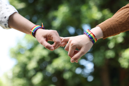 LGBT concept. Women in rainbow wristbands holding hands outdoors, closeup