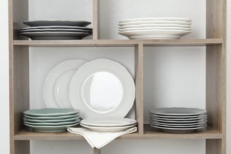 Shelving unit with different plates near white wall indoors
