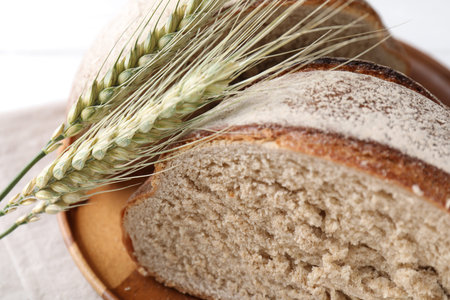 Pieces of fresh bread and green wheat spikes on white table, closeup