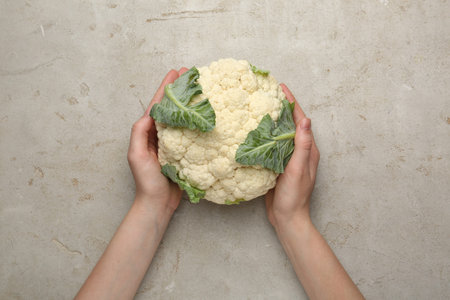 Woman with whole cauliflower at light table, top view