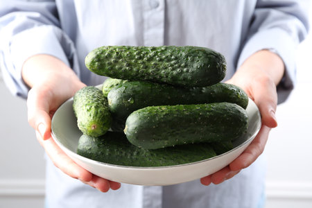 Woman with bowl of fresh cucumbers near white wall, closeupの写真素材