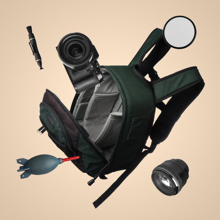 Photographer's backpack and professional equipment flying against dark beige background