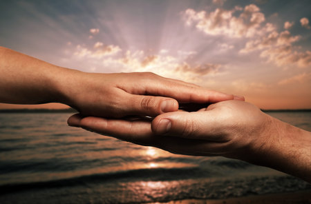 Man and woman holding hands against seascape at sunset, closeup
