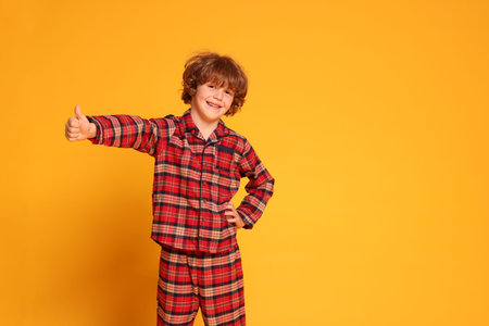 Cute little boy in pajamas showing thumbs up on yellow background. Space for textの写真素材