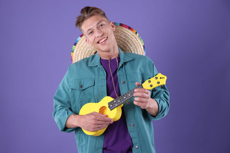 Happy man with sombrero hat playing ukulele on purple background