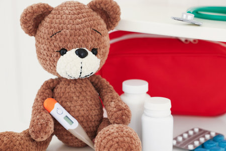 Pediatrics concept. Toy bear with thermometer and pills on white background