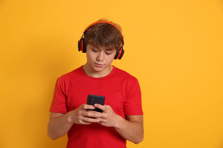 Teenage boy in headphones using smartphone on yellow background