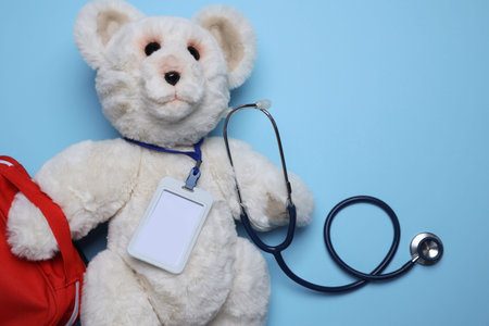 Pediatrics concept. Toy bear with stethoscope and first aid kit on light blue background, top view....