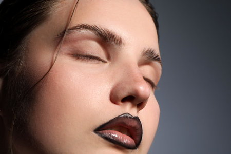 Beautiful young woman with black lip liner on light grey background, closeup