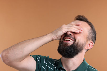 Man covering eyes and laughing on brown backgroundの写真素材