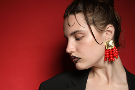 Beautiful young woman with black lip liner wearing stylish earrings on dark red background, closeup. Space for textの写真素材