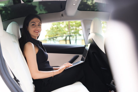 Woman using laptop in modern car, view from outside