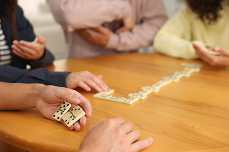 Friends playing dominoes at wooden table, closeup
