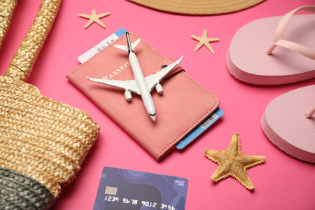 Airplane model, passport, flight ticket, credit card, and beach accessories on pink background,...