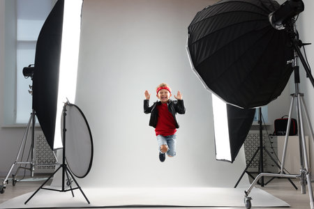Little boy on light gray background in photo studio with professional equipmentの写真素材