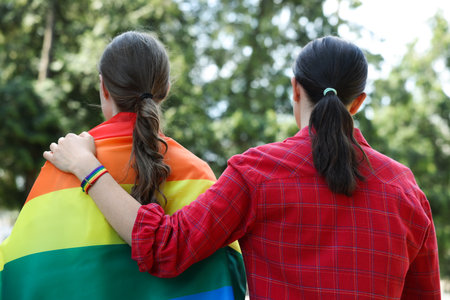 LGBT concept. Women in rainbow wristband with flag outdoors, back viewの写真素材
