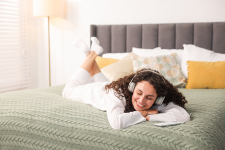 Young woman with headphones listening to music on bed at homeの写真素材