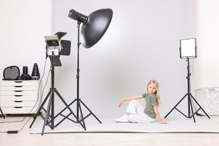 Little girl on light grey background in photo studio with professional equipment